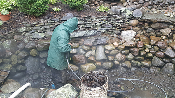 Pond Crew Member Standing In Drained Pond Pressue Washing Rocks